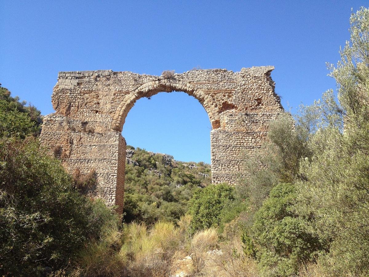 The arch of a Roman aqueduct ruin standing among greenery in Kumkuyu