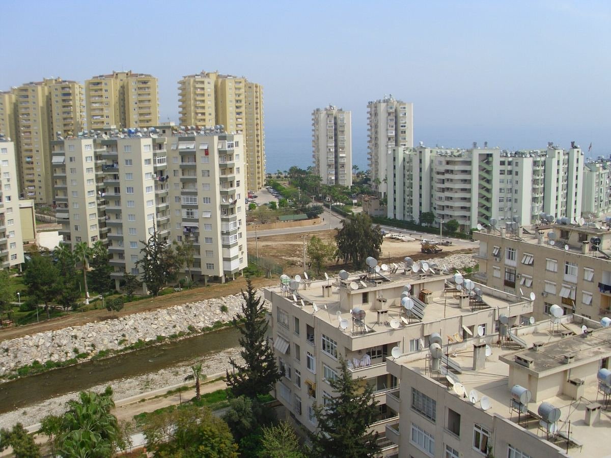 Mezitli'de Viranşehir çevresinde apartmanlar, dere yatağı ve arkada Akdeniz